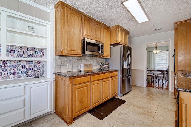 kitchen with a textured ceiling, stainless steel appliances, visible vents, brown cabinets, and dark stone countertops