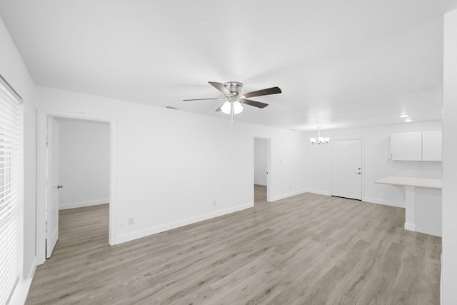 spare room featuring ceiling fan with notable chandelier, light wood-type flooring, visible vents, and baseboards