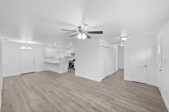 unfurnished living room with ceiling fan with notable chandelier, baseboards, and light wood-style floors