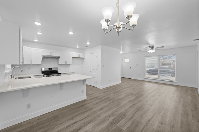 kitchen featuring a peninsula, stainless steel electric stove, light countertops, under cabinet range hood, and a sink