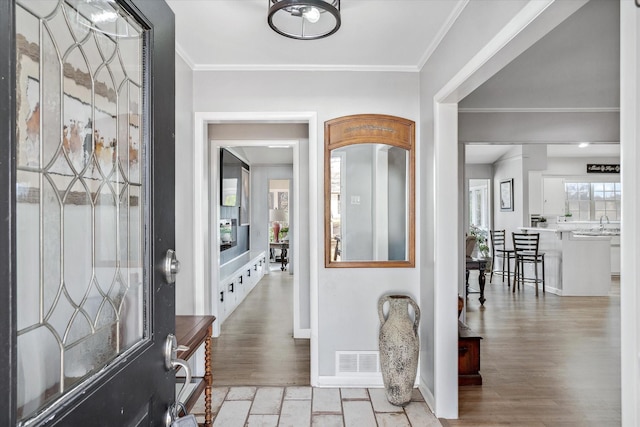 foyer entrance featuring baseboards, light wood-style flooring, visible vents, and crown molding