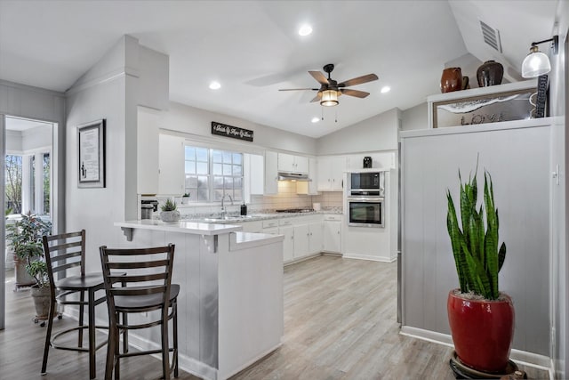 kitchen featuring a peninsula, vaulted ceiling, light countertops, under cabinet range hood, and a sink