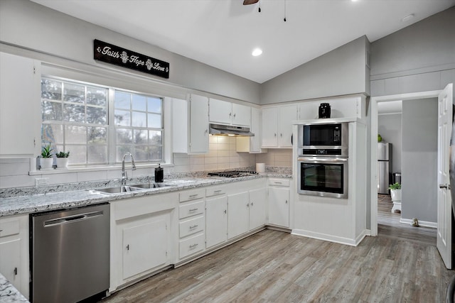 kitchen featuring vaulted ceiling, stainless steel appliances, under cabinet range hood, white cabinetry, and a sink