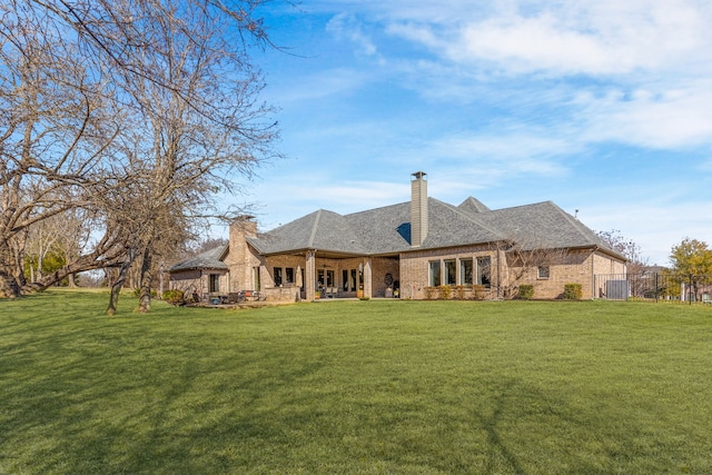 back of property with brick siding, fence, a lawn, a chimney, and a patio area