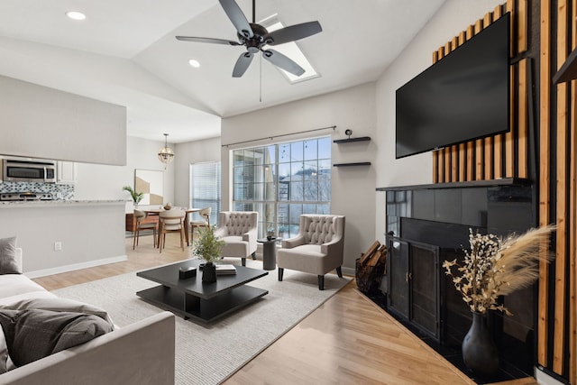 living room featuring a fireplace, baseboards, vaulted ceiling, and wood finished floors