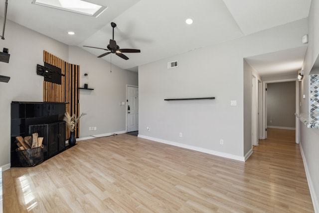 unfurnished living room with vaulted ceiling with skylight, visible vents, baseboards, light wood-style flooring, and a fireplace