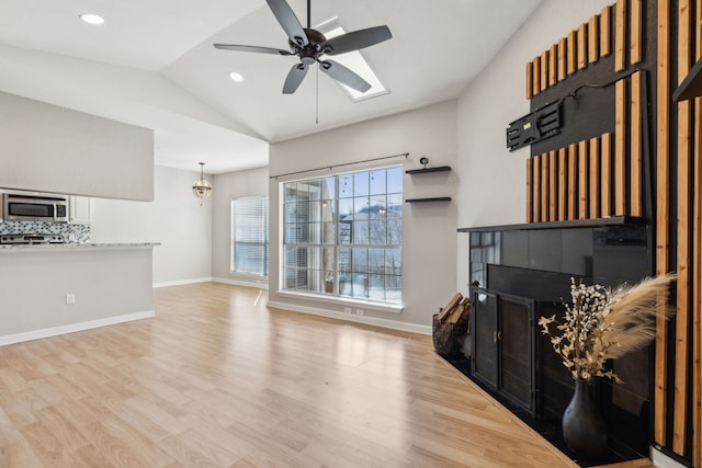 living room featuring a ceiling fan, vaulted ceiling, baseboards, and wood finished floors