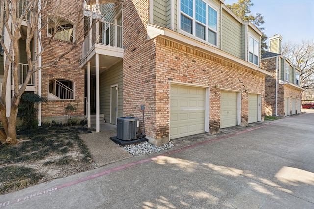 view of side of home with central air condition unit, an attached garage, aphalt driveway, and brick siding