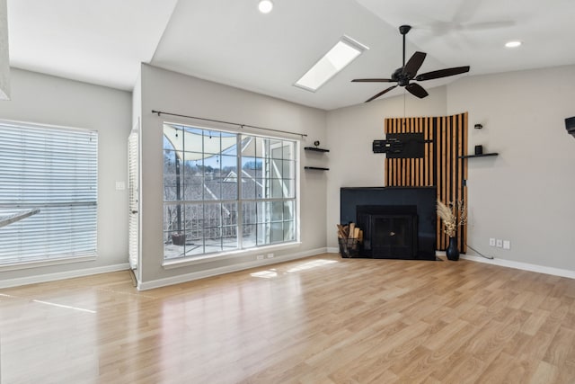 unfurnished living room featuring vaulted ceiling with skylight, a fireplace, baseboards, and wood finished floors