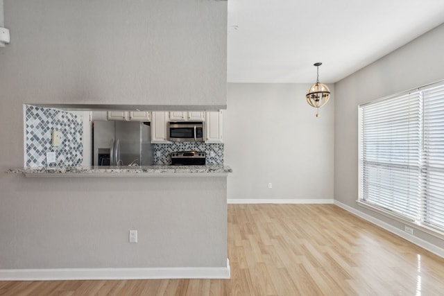 kitchen with a notable chandelier, white cabinetry, light wood-style floors, appliances with stainless steel finishes, and backsplash