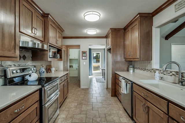 kitchen with under cabinet range hood, stainless steel appliances, a sink, baseboards, and stone finish flooring