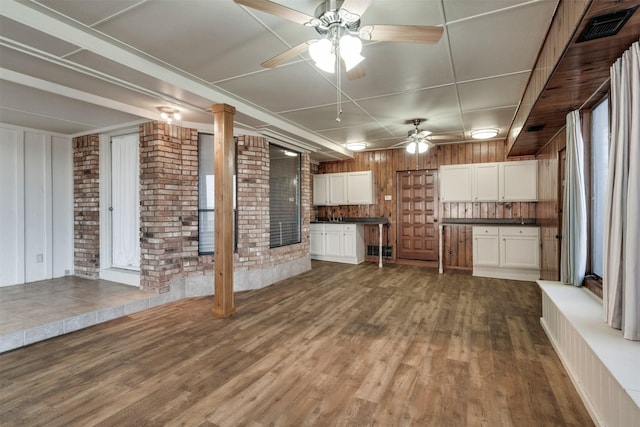 interior space featuring brick wall, dark wood-style flooring, visible vents, white cabinets, and dark countertops