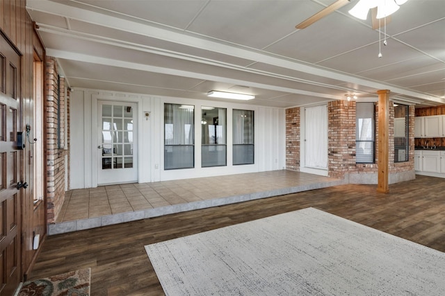 interior space with brick wall, dark wood-type flooring, beam ceiling, and a ceiling fan