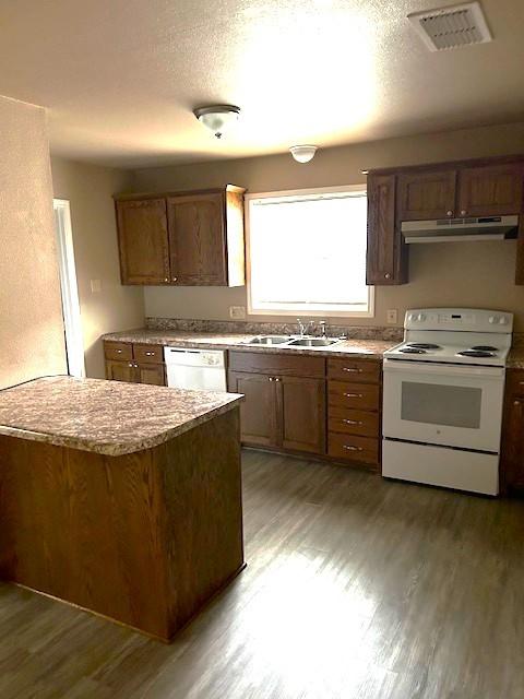 kitchen featuring visible vents, a sink, wood finished floors, white appliances, and under cabinet range hood