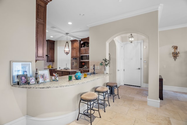 kitchen with arched walkways, a breakfast bar area, a peninsula, ornamental molding, and built in microwave