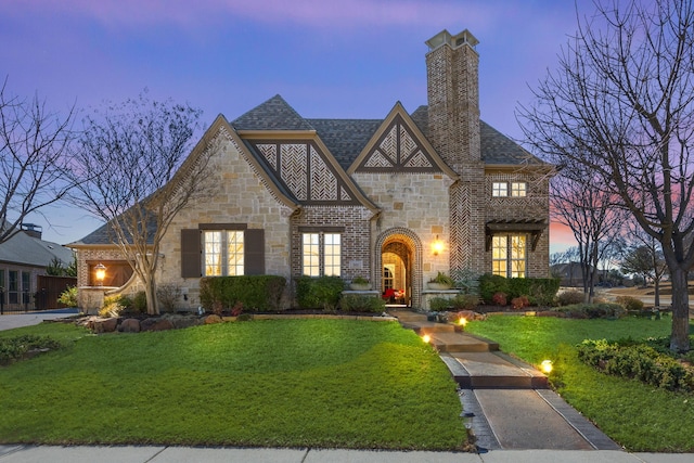 tudor house with brick siding, a lawn, a chimney, and a shingled roof