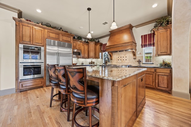 kitchen featuring light wood finished floors, brown cabinetry, tasteful backsplash, and built in appliances