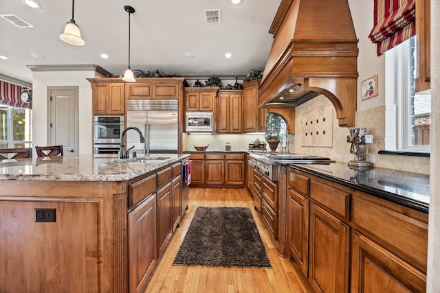 kitchen featuring a kitchen island with sink, brown cabinetry, visible vents, and built in appliances