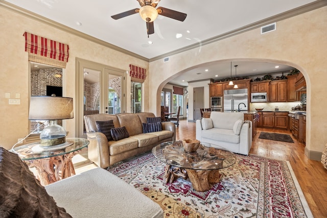 living room featuring visible vents, arched walkways, ornamental molding, and light wood finished floors