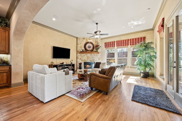 living room featuring a ceiling fan, arched walkways, light wood-style floors, a fireplace, and crown molding