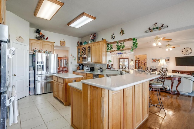 kitchen featuring stainless steel refrigerator with ice dispenser, light countertops, glass insert cabinets, a sink, and a peninsula