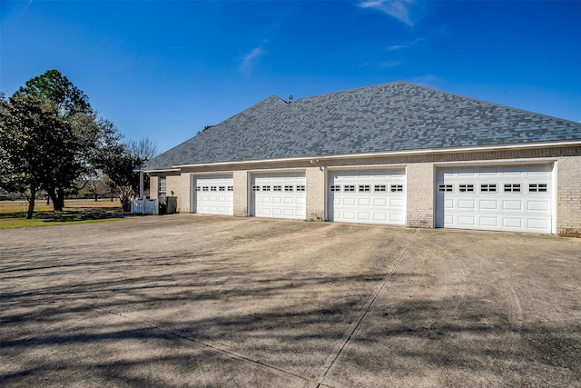 view of side of home featuring a garage, roof with shingles, and brick siding