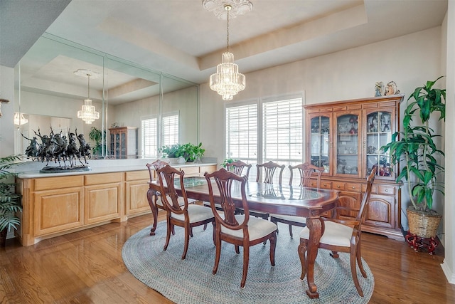 dining space featuring a raised ceiling, light wood-style flooring, and an inviting chandelier