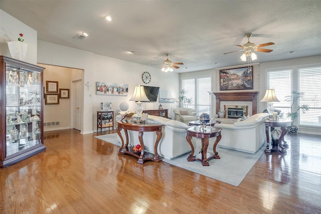 living area with a ceiling fan, a fireplace, visible vents, and light wood-style floors