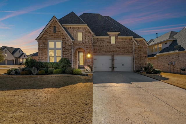 view of front facade with driveway, a garage, roof with shingles, a yard, and brick siding