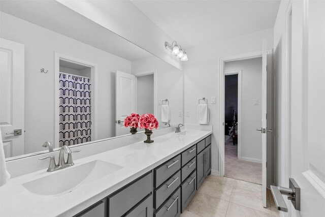 full bath with baseboards, double vanity, tile patterned floors, and a sink