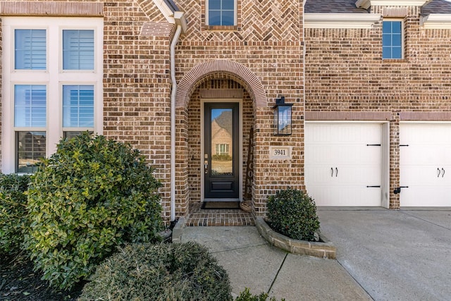 view of exterior entry featuring a shingled roof, concrete driveway, and brick siding