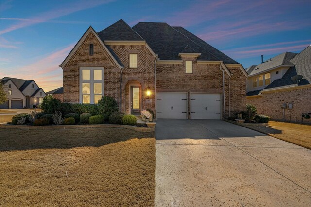 view of front facade with a shingled roof, brick siding, a garage, a front yard, and driveway