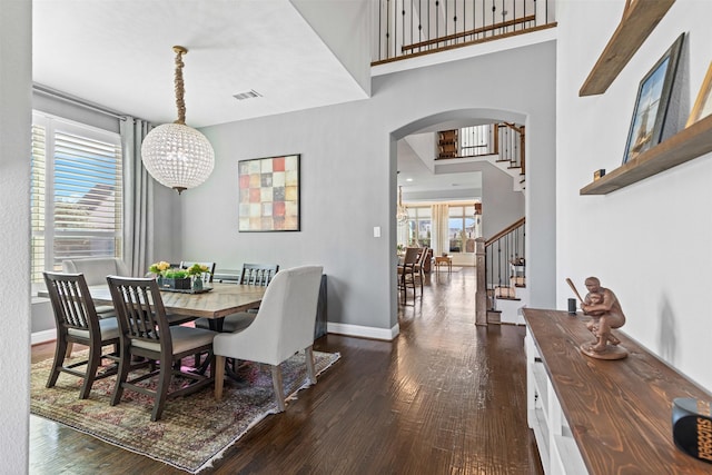 dining room with baseboards, visible vents, a towering ceiling, stairway, and dark wood-type flooring