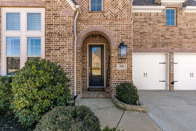 view of exterior entry with concrete driveway, brick siding, and an attached garage