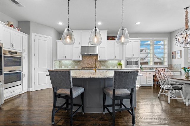 kitchen featuring under cabinet range hood, dark wood-type flooring, visible vents, white cabinets, and appliances with stainless steel finishes