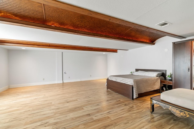 bedroom featuring light wood-type flooring, visible vents, baseboards, and beam ceiling