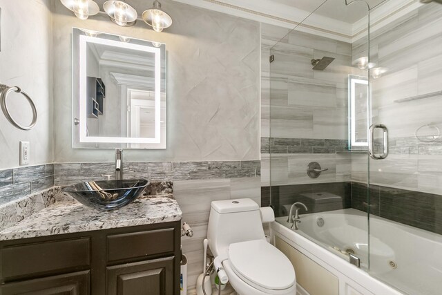 full bathroom featuring bath / shower combo with glass door, toilet, ornamental molding, vanity, and tile walls