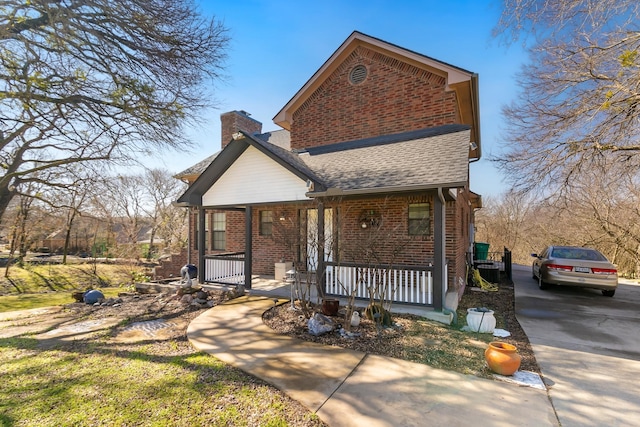 view of front of property with covered porch, brick siding, a chimney, and a shingled roof