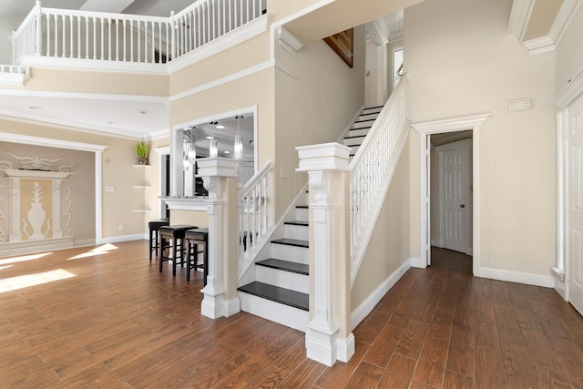 staircase with wood-type flooring, a high ceiling, baseboards, and ornamental molding