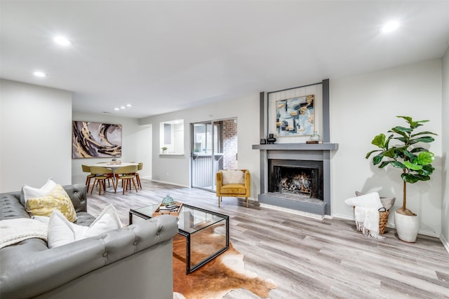 living room featuring a fireplace with raised hearth, baseboards, wood finished floors, and recessed lighting