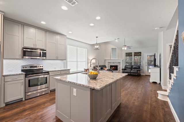 kitchen with stainless steel appliances, visible vents, a sink, vaulted ceiling, and a warm lit fireplace