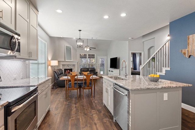 kitchen featuring dark wood-style flooring, stainless steel appliances, decorative backsplash, a sink, and a stone fireplace