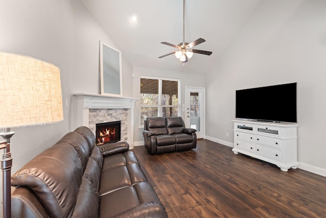 living area featuring ceiling fan, a stone fireplace, wood finished floors, high vaulted ceiling, and baseboards