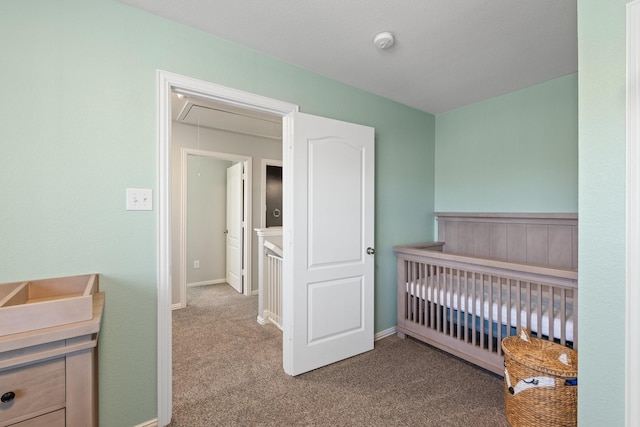 bedroom featuring a crib, attic access, baseboards, and carpet flooring