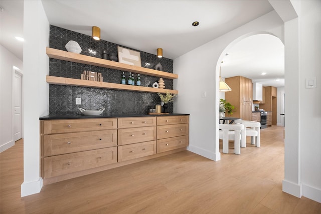 bar featuring arched walkways, stainless steel range with gas cooktop, light wood finished floors, decorative backsplash, and baseboards