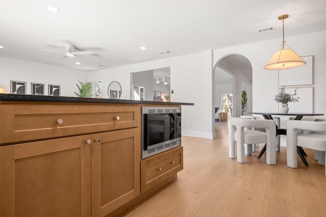 kitchen with arched walkways, built in microwave, dark countertops, visible vents, and light wood-type flooring