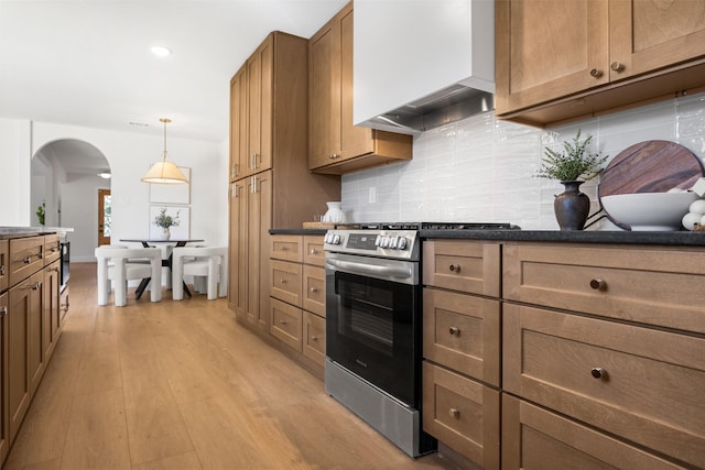 kitchen featuring arched walkways, wall chimney range hood, dark countertops, and gas range