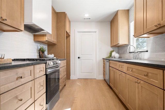 kitchen featuring dark countertops, wall chimney exhaust hood, appliances with stainless steel finishes, light wood-type flooring, and a sink