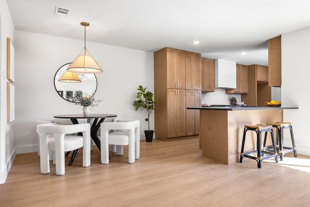 kitchen featuring a breakfast bar, tasteful backsplash, dark countertops, visible vents, and light wood-style floors