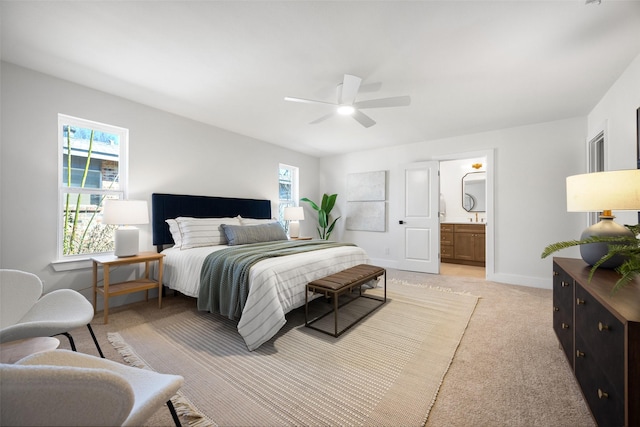 bedroom featuring light carpet, ceiling fan, baseboards, and ensuite bathroom